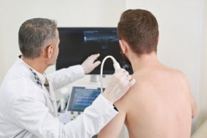 Echografisch onderzoek bij tendinitis calcarea: de echokop op de schouder om de kalkafzetting in de supraspinatuspees in beeld te brengen